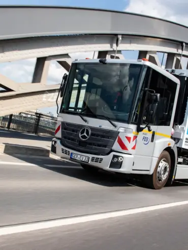 Elektrischer Lkw Mercedes-Benz eEconic fährt über eine Brücke in einer urbanen Umgebung.