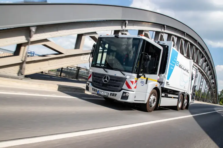 Elektrischer Lkw Mercedes-Benz eEconic fährt über eine Brücke in einer urbanen Umgebung.