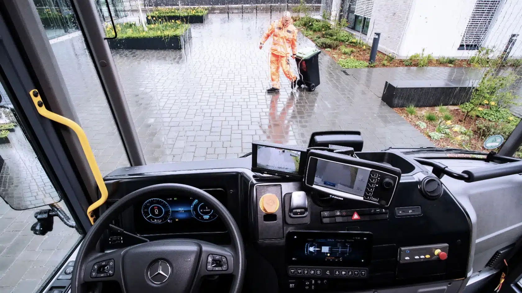 Innenansicht der Kabine eines Mercedes-Benz eEconic mit modernem Cockpit und Blick auf eine Person in orangefarbener Arbeitskleidung im Stadtgebiet.