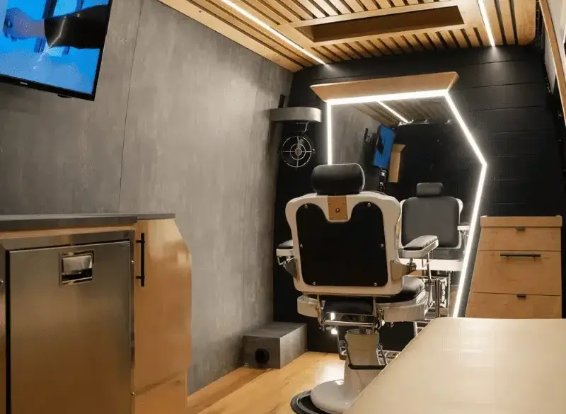 Innenraum eines umgebauten Mercedes Sprinter als mobiler Barbershop mit Barberstuhl, großem Spiegel, TV und moderner Ausstattung.