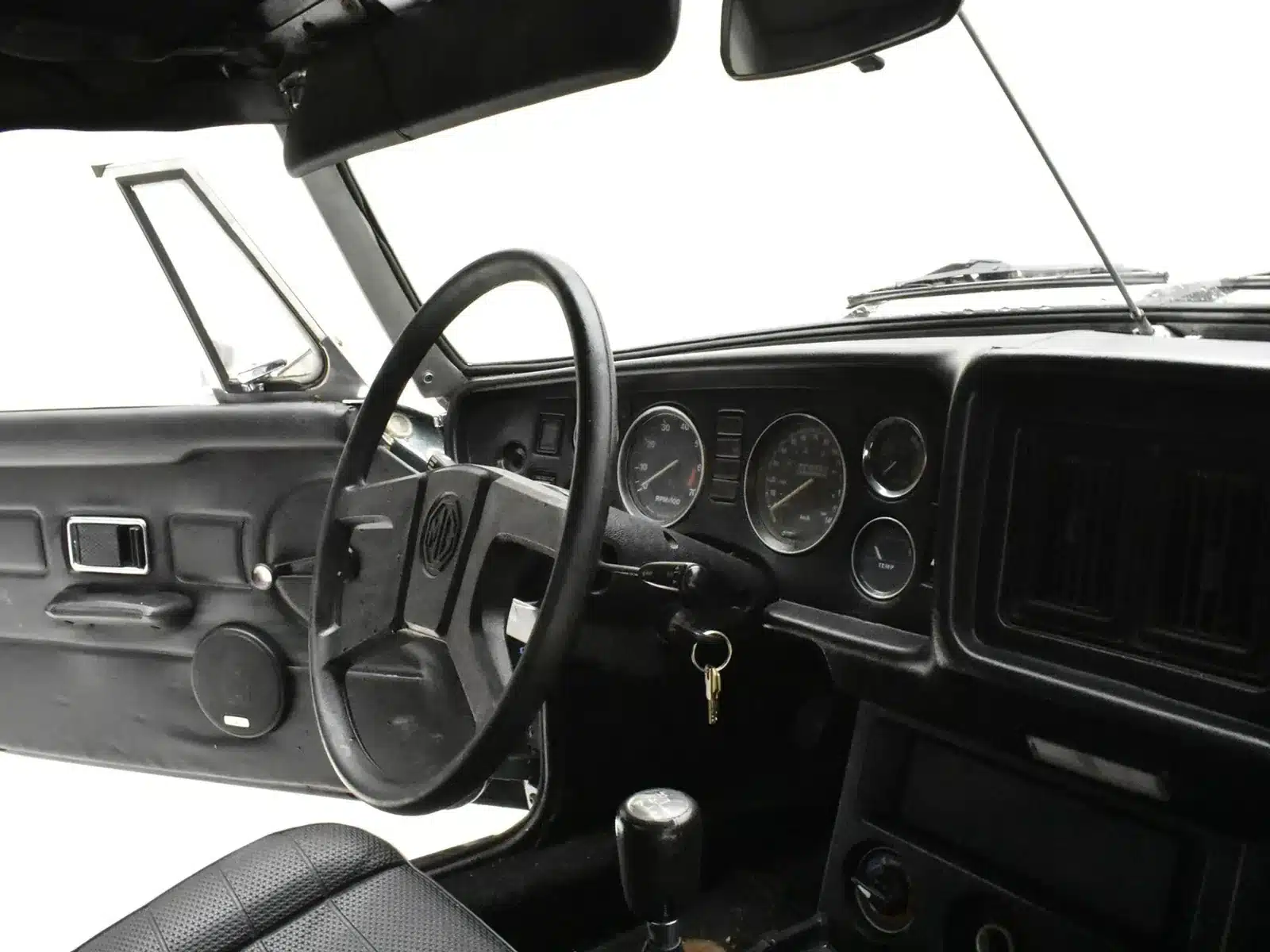 Blick auf das schwarze Interieur und Armaturenbrett eines MGB Roadster von 1980 mit Lenkrad, Instrumenten und Schaltknauf.
