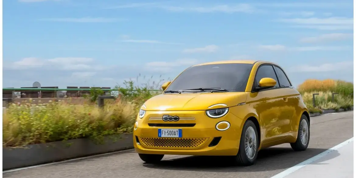 Gelber Fiat 500 Hybrid fährt auf einer Straße im Stadtumfeld bei Tageslicht