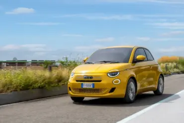 Gelber Fiat 500 Hybrid fährt auf einer Straße im Stadtumfeld bei Tageslicht