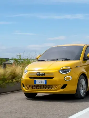 Gelber Fiat 500 Hybrid fährt auf einer Straße im Stadtumfeld bei Tageslicht