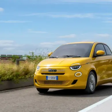 Gelber Fiat 500 Hybrid fährt auf einer Straße im Stadtumfeld bei Tageslicht
