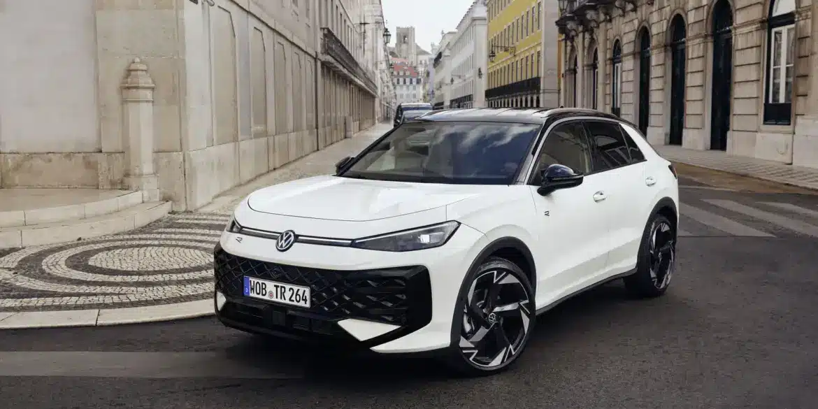 VW T-Roc Kompakt-SUV in weiß auf einer Stadtstraße, mit moderner Architektur im Hintergrund