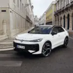 VW T-Roc Kompakt-SUV in weiß auf einer Stadtstraße, mit moderner Architektur im Hintergrund