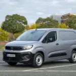 Opel Combo Electric Transporter in Silber auf einem Parkplatz vor städtischer Kulisse.