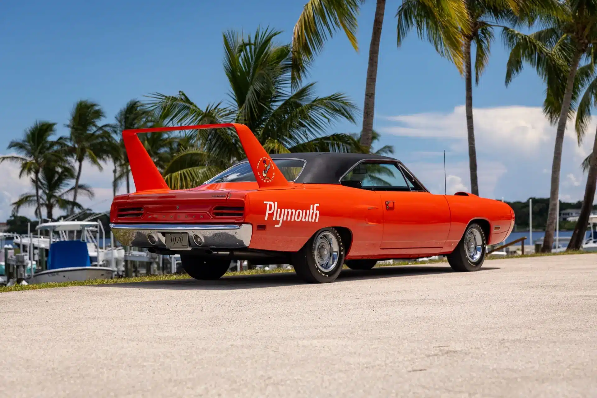 Heckansicht eines orangefarbenen 1970 Plymouth Superbird mit gigantischem Heckflügel und Plymouth-Schriftzug, im Freien vor Palmen.