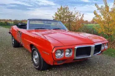 Pontiac Firebird Cabriolet 1969, orange lackiert, mit geöffnetem Verdeck und charakteristischer Front, stehend auf einem ländlichen Weg.
