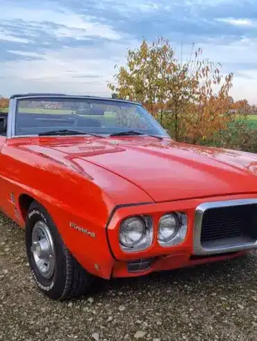 Pontiac Firebird Cabriolet 1969, orange lackiert, mit geöffnetem Verdeck und charakteristischer Front, stehend auf einem ländlichen Weg.