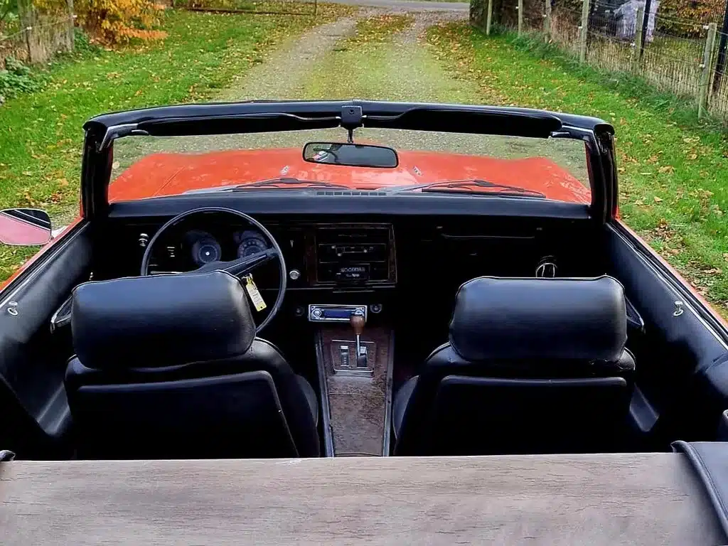 Innenraum eines Pontiac Firebird Cabriolet 1969 – schwarzes Interieur, Lenkrad und Mittelkonsole sichtbar, Verdeck geöffnet.