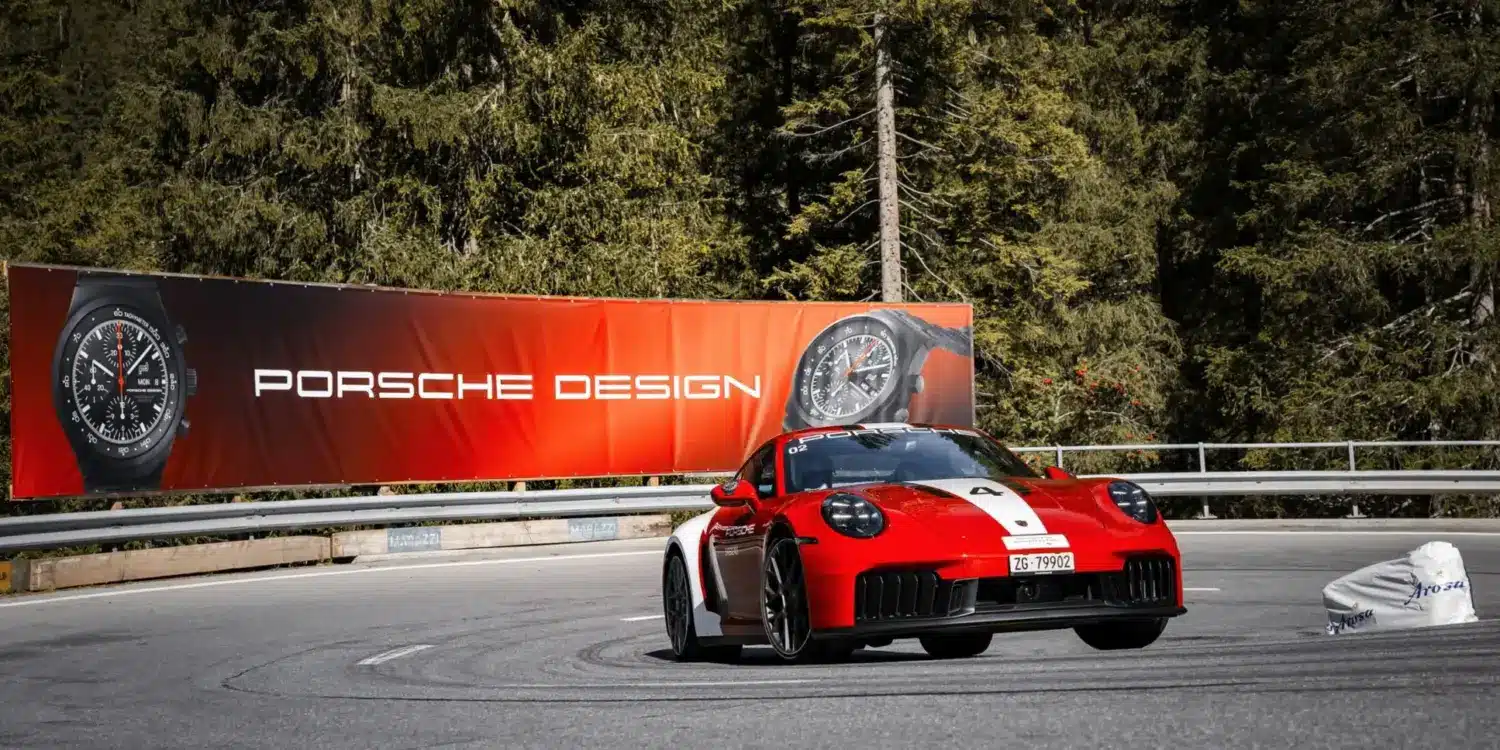 Porsche 911 Carrera GTS auf Bergstraße mit Werbebanner für Porsche Design Chronographen im Hintergrund