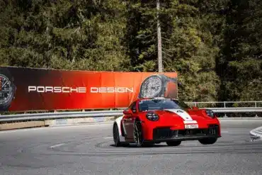 Porsche 911 Carrera GTS auf Bergstraße mit Werbebanner für Porsche Design Chronographen im Hintergrund