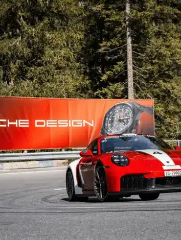 Porsche 911 Carrera GTS auf Bergstraße mit Werbebanner für Porsche Design Chronographen im Hintergrund