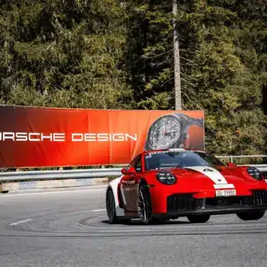 Porsche 911 Carrera GTS auf Bergstraße mit Werbebanner für Porsche Design Chronographen im Hintergrund
