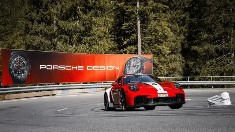 Porsche 911 Carrera GTS auf Bergstraße mit Werbebanner für Porsche Design Chronographen im Hintergrund