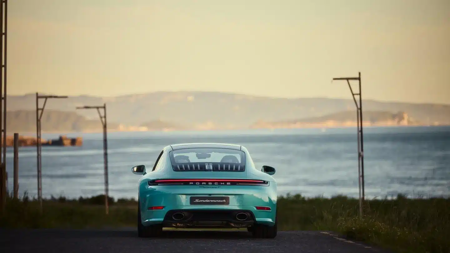 Heckansicht des Porsche 911 Carrera T Formosa in Ipanema Blue Metallic an einer Küstenstraße mit Meerblick.