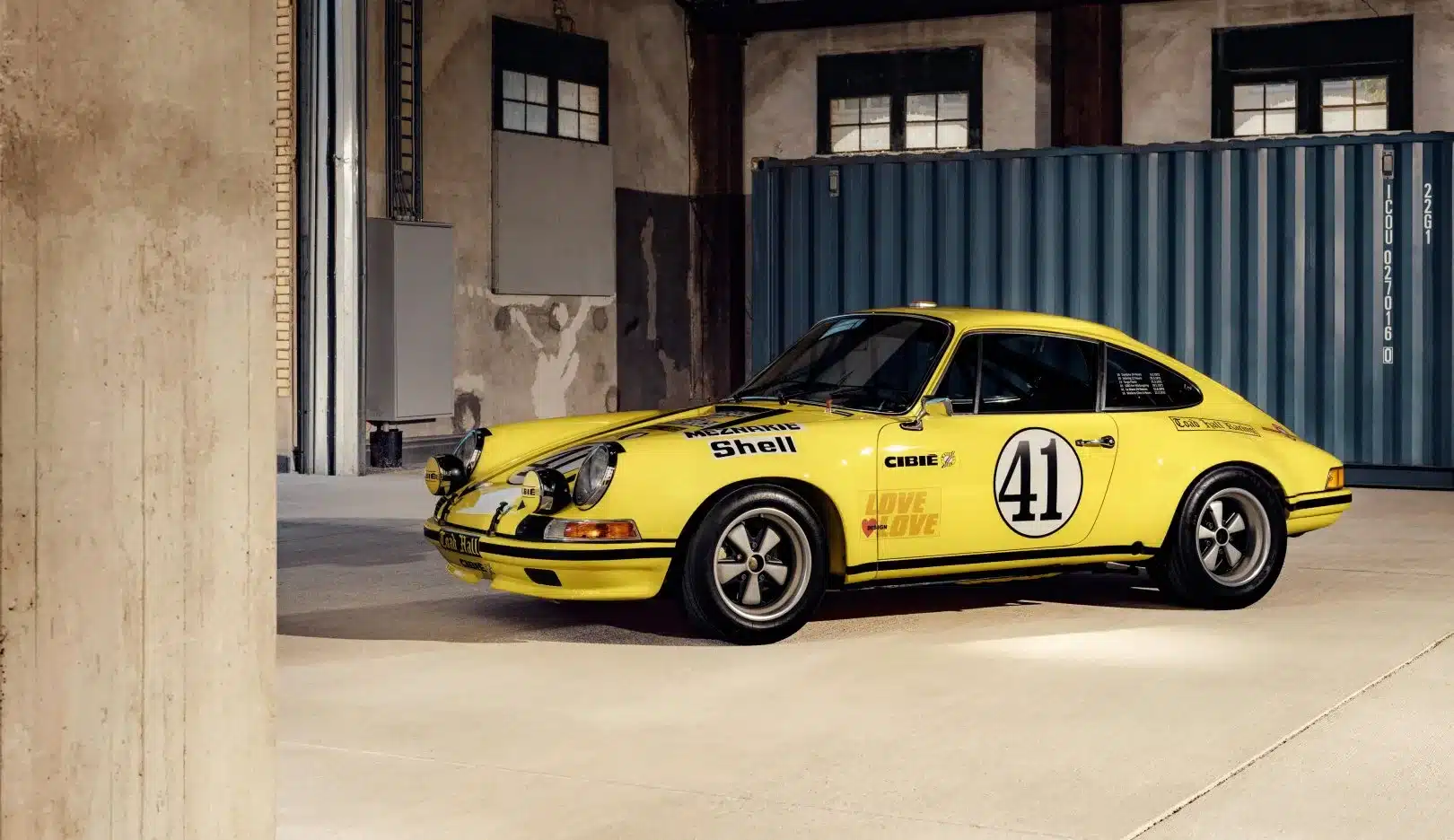 Seitenansicht eines gelben Porsche 911 2.5 S/T mit Startnummer 41 und Rennbeklebung, stehend in einer Halle