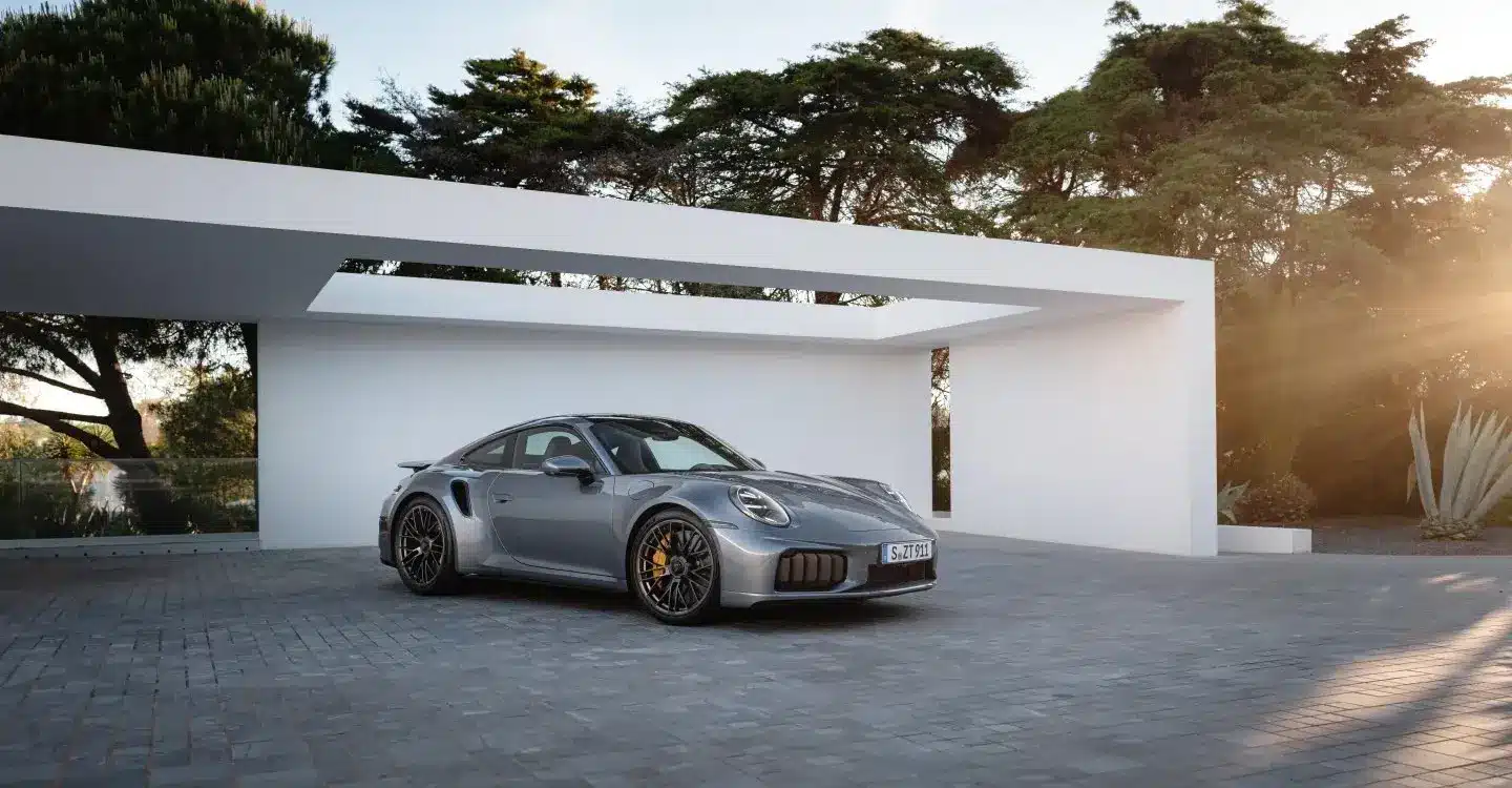 Porsche 911 Turbo S Performance-Hybrid 2025 in Silber vor moderner Garage bei Sonnenuntergang