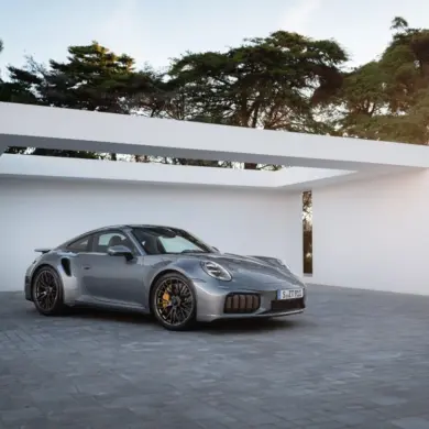 Porsche 911 Turbo S Performance-Hybrid 2025 in Silber vor moderner Garage bei Sonnenuntergang