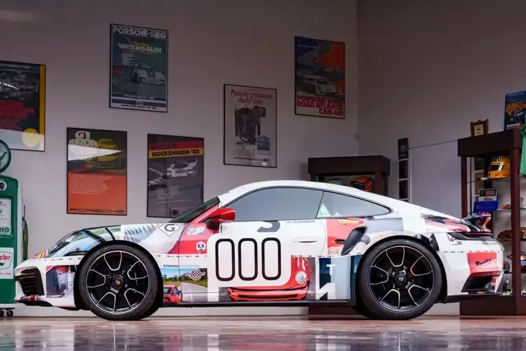 Seitenansicht eines Porsche 911 Turbo S Lightweight 2022 mit auffälligem Motorsport-Design in einer stilvollen Garage.