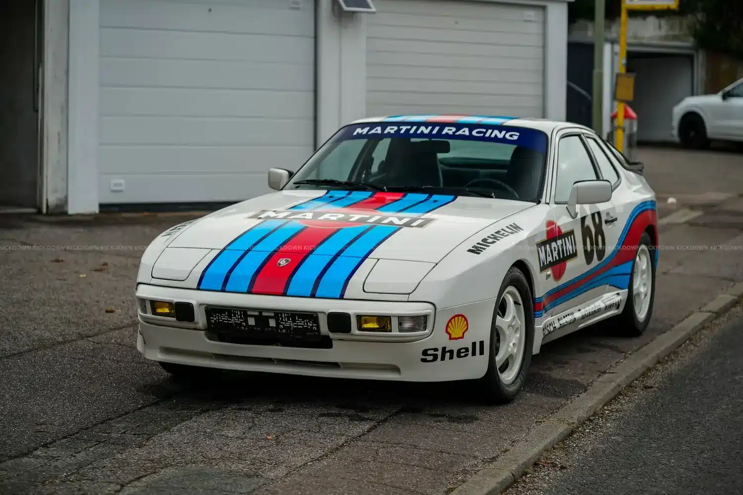 Weißer Porsche 944 Baujahr 1986 mit Martini-Racing-Beklebung und Startnummer 68, geparkt vor einer Garage.