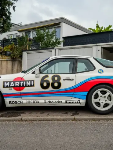 Porsche 944 von 1986, weiß mit Martini-Racing-Folierung, seitlich fotografiert vor Garagen