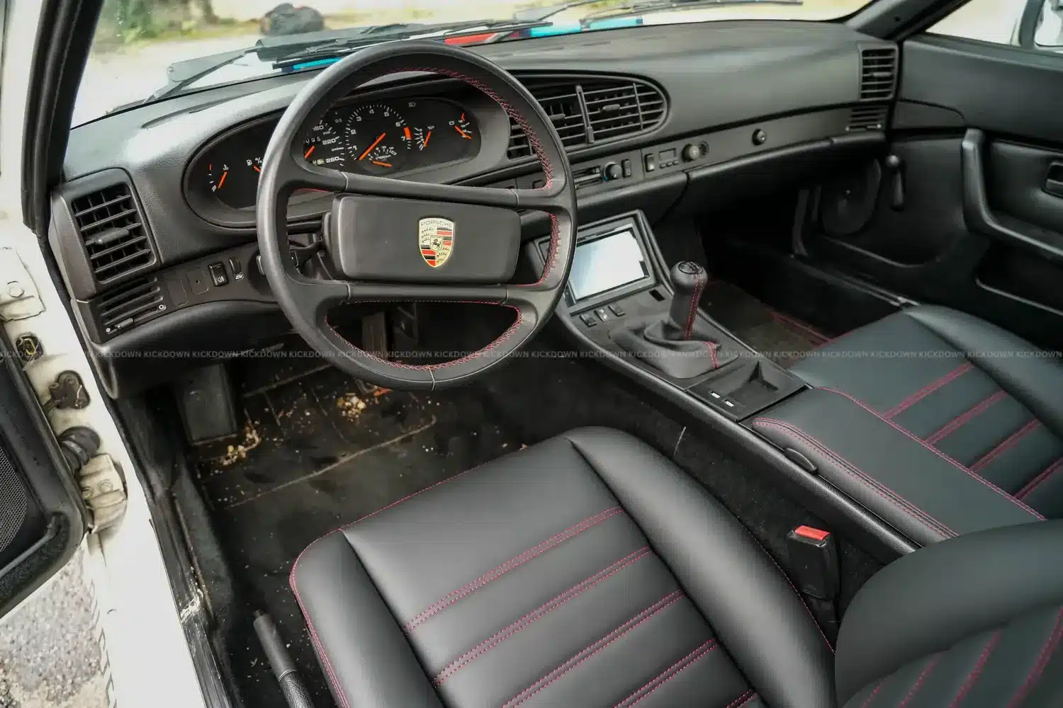 Innenraum eines Porsche 944, schwarze Lederausstattung mit roten Ziernähten, Blick auf Lenkrad, Schaltung und Armaturenbrett