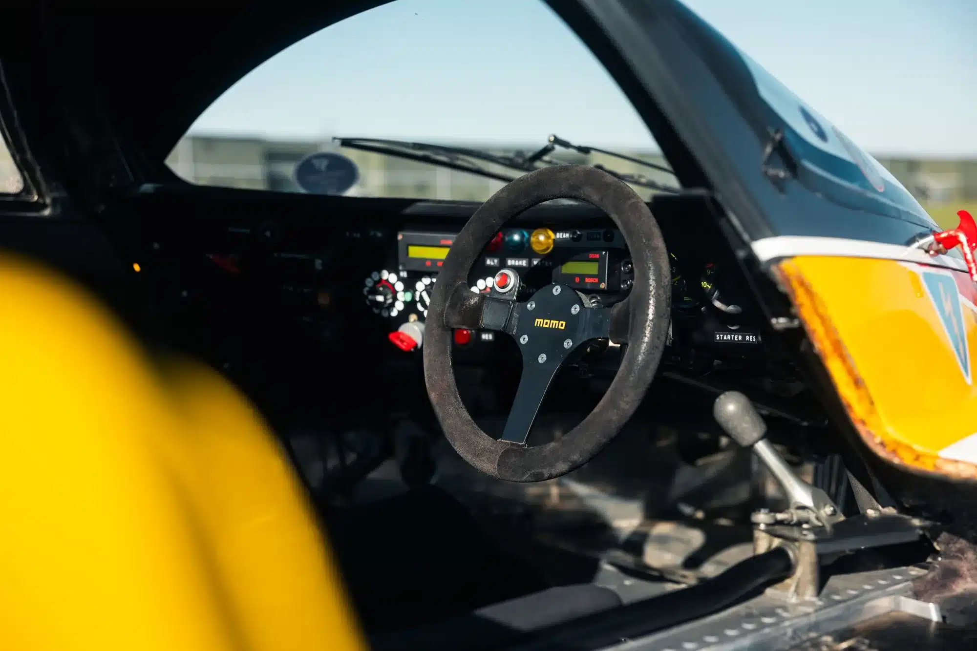 Innenraumansicht des Cockpits der Porsche 962-010, zeigt das MOMO-Lenkrad und Bedienelemente im historischen Rennwagen.