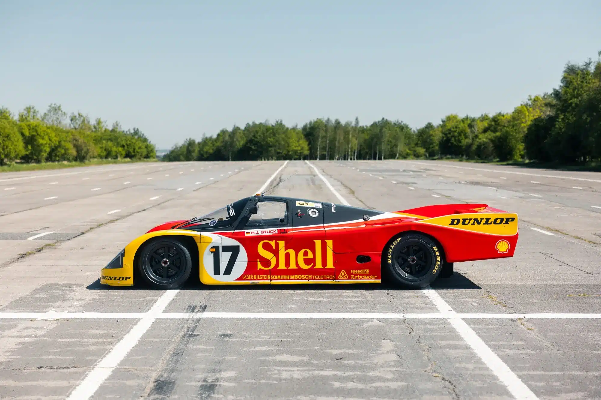 Porsche 962-010 in Shell/Dunlop-Renndesign seitlich auf einer leeren Teststrecke
