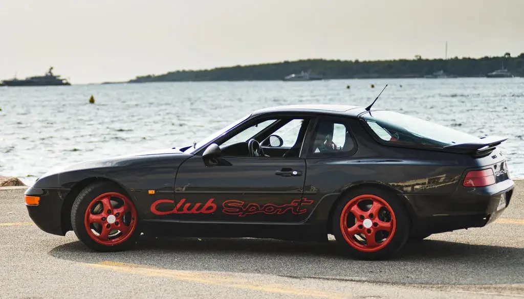 Porsche 968 Club Sport in Schwarz mit roten Cup-Felgen am Wasser geparkt