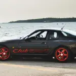 Porsche 968 Club Sport in Schwarz mit roten Cup-Felgen am Wasser geparkt