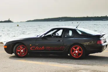 Porsche 968 Club Sport in Schwarz mit roten Cup-Felgen am Wasser geparkt