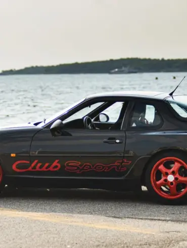 Porsche 968 Club Sport in Schwarz mit roten Cup-Felgen am Wasser geparkt