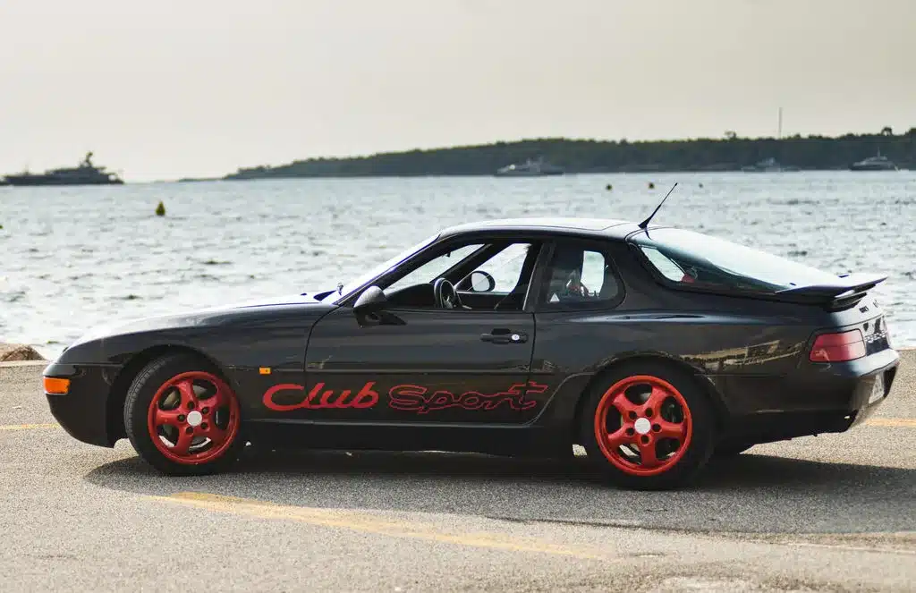 Porsche 968 Club Sport in Schwarz mit roten Cup-Felgen am Wasser geparkt