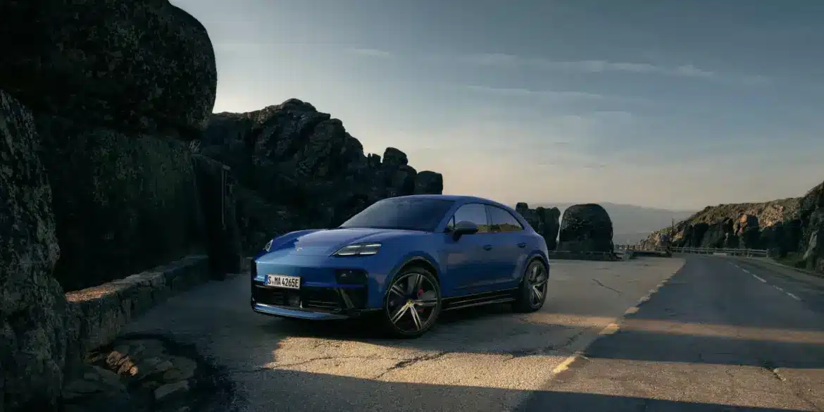 Blauer Porsche Macan GTS Electric auf einer Straße in den Bergen, seitliche Frontansicht, sportliches Design, schwarze Akzente.