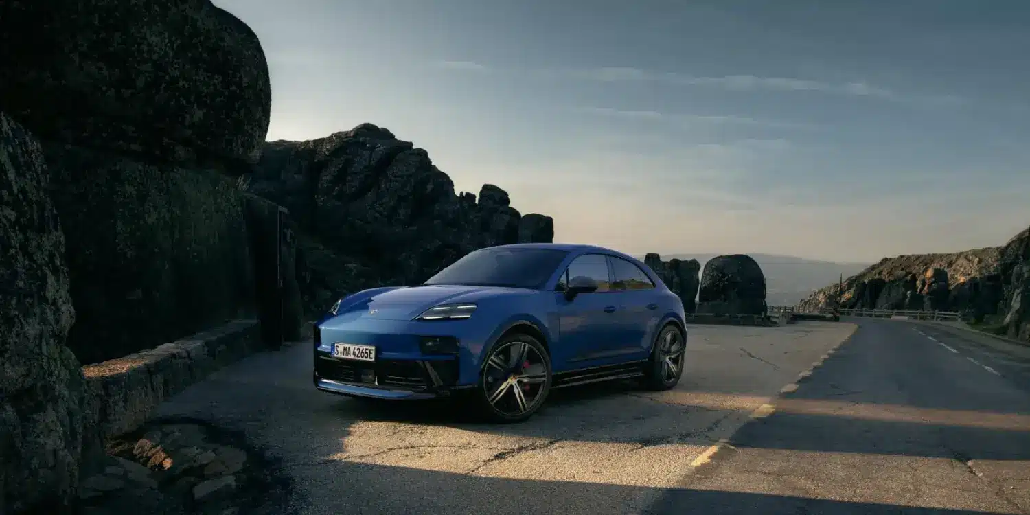 Blauer Porsche Macan GTS Electric auf einer Straße in den Bergen, seitliche Frontansicht, sportliches Design, schwarze Akzente.