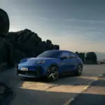 Blauer Porsche Macan GTS Electric auf einer Straße in den Bergen, seitliche Frontansicht, sportliches Design, schwarze Akzente.