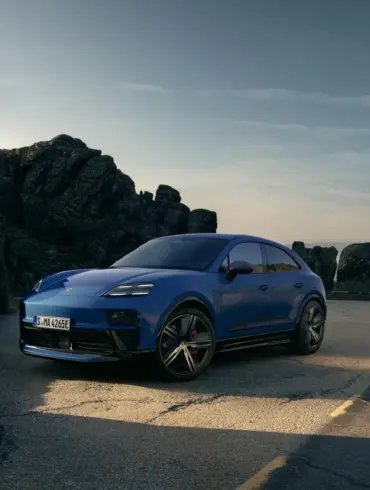 Blauer Porsche Macan GTS Electric auf einer Straße in den Bergen, seitliche Frontansicht, sportliches Design, schwarze Akzente.