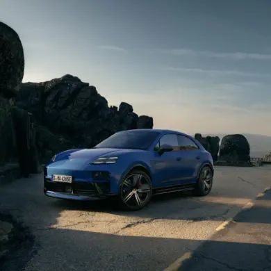Blauer Porsche Macan GTS Electric auf einer Straße in den Bergen, seitliche Frontansicht, sportliches Design, schwarze Akzente.