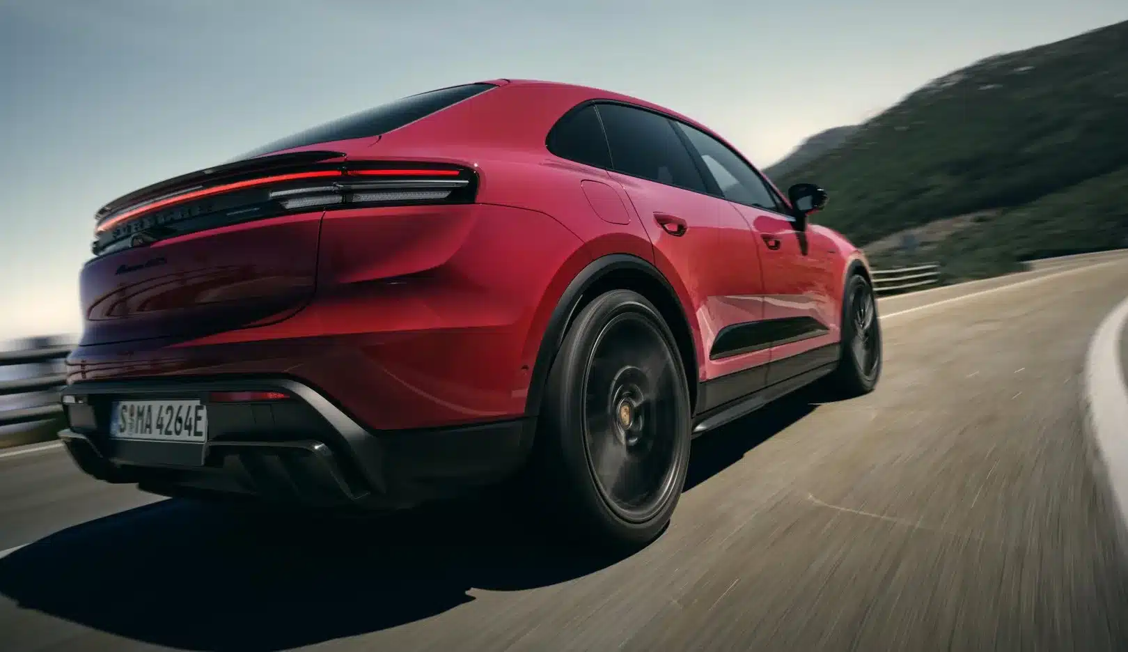 Heckansicht eines roten Porsche Macan GTS Electric beim sportlichen Fahren auf einer Straße.