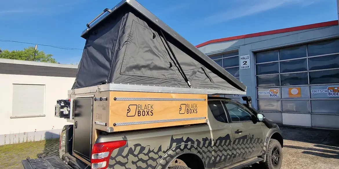 Pickup mit montierter PUR Camperkabine und aufgeklapptem Aufstelldach auf einem Firmengelände