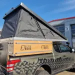 Pickup mit montierter PUR Camperkabine und aufgeklapptem Aufstelldach auf einem Firmengelände