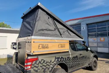 Pickup mit montierter PUR Camperkabine und aufgeklapptem Aufstelldach auf einem Firmengelände