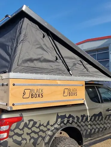 Pickup mit montierter PUR Camperkabine und aufgeklapptem Aufstelldach auf einem Firmengelände