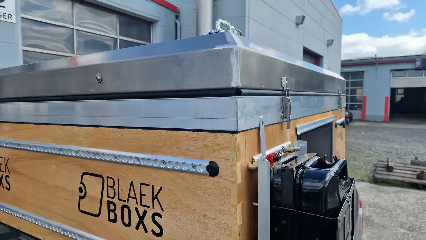 PUR Camperkabine mit Aluminium-Aufstelldach und hölzernem Korpus, aufgenommen an einem Pickup neben Industriegebäude.