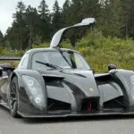 Frontansicht eines Radical RXC TwinTurbo GT 650R mit geöffneter Fahrertür, Kohlefaser-Karosserie, auf einer Straße vor bewaldetem Hintergrund