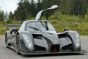 Frontansicht eines Radical RXC TwinTurbo GT 650R mit geöffneter Fahrertür, Kohlefaser-Karosserie, auf einer Straße vor bewaldetem Hintergrund