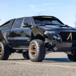 Apocalypse Juggernaut 6x6 Pickup, schwarz, mit sechs großen Offroad-Rädern, breiten Kotflügeln und massiver Front im Freien stehend.